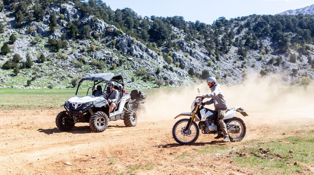Buggy and dirt bike kicking up dust on a mountain trail