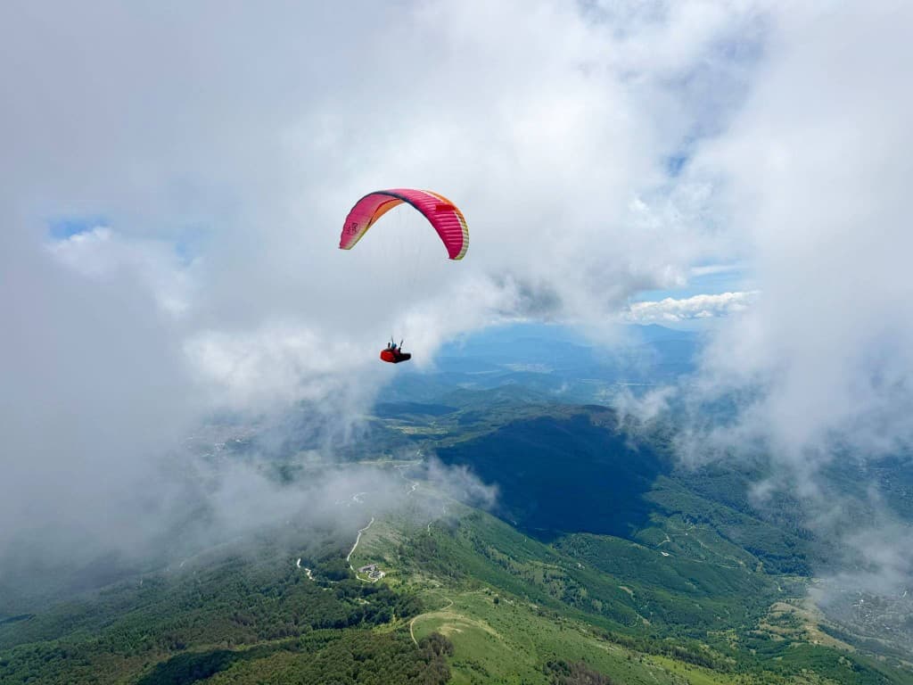 Paraglider soaring high above green mountain ridges