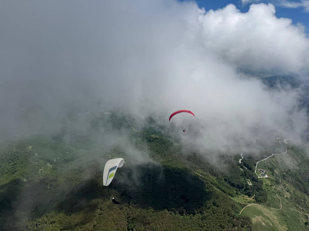 Pilot gliding between the clouds over forested hills