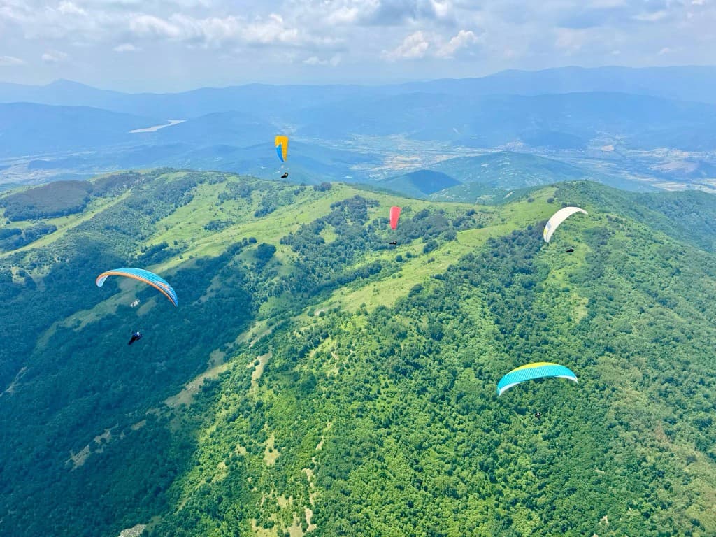 Paraglider above misty green mountains