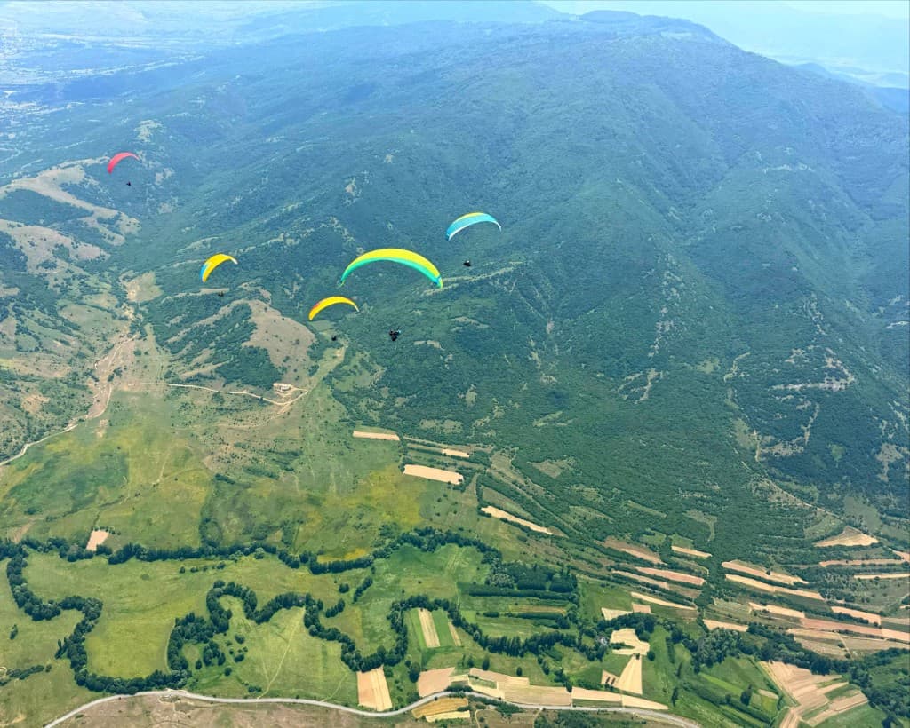 Paragliders scattered across a vast green valley